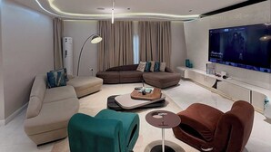 Una sala de estar moderna con un televisor de pantalla plana grande, un sofá marrón, un pouf color turquesa y una mesa de centro.