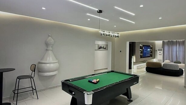 Una mesa de billar moderna en interior, con superficie de fieltro verde, rodeada de un suelo limpio de baldosas blancas.