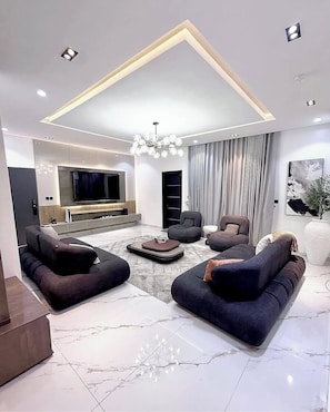 Ein modernes Wohnzimmer mit großem Fernseher, dunklen Sofas und einer Chandelüster.