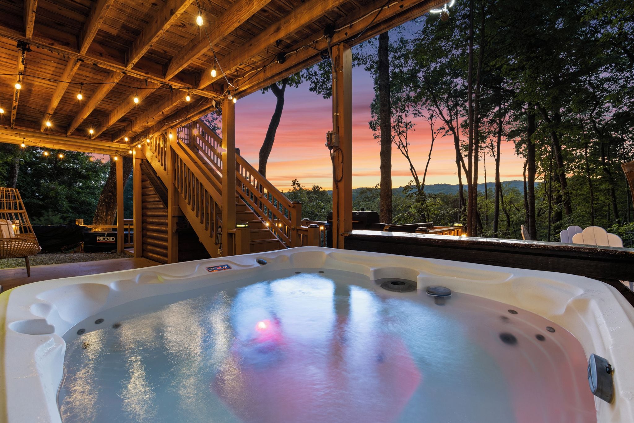 Ein Whirlpool mit einer Holzterrasse und Treppe, umgeben von Bäumen und Blick auf den Sonnenuntergang.