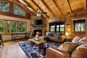 L’intérieur d’un chalet est agrémenté d’une cheminée en pierre, de meubles en cuir et de grandes fenêtres qui offrent une vue sur le paysage extérieur.