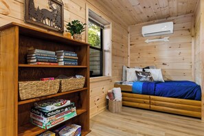 Ein gemütliches Zimmer mit einer Holzbücherreih, einem Bett mit blauer Decke und einem Fenster mit Klimaanlage.