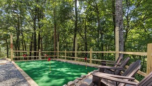 A miniature golf course with a wooden fence, green artificial turf, and wooden chairs. - Mountain View Cabin | Theatre & Game Room | Hot Tub (Blue Ridge)