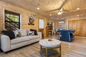 Ein Holzinnenraum mit einer Couch, Hocker, Deckenventilator und einem aufgehängten Hirschkopf.