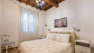 Une chambre à coucher avec un lit, une chaise, une table de chevet, une lampe et un tableau au mur.