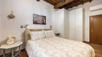 A bedroom with a bed, a nightstand, a decorative angel, a painting, and a wardrobe.
