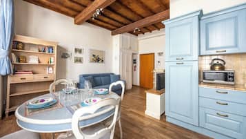 Un coin repas avec une table ronde, des chaises et un canapé bleu. La cuisine est équipée de meubles bleus et d’un four à micro-ondes.