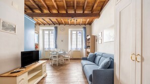 Een kamer met een houten plafond, een blauwe bank, een televisie op een houten kast en een eettafel met stoelen.