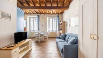 Une pièce avec un plafond en bois, un canapé bleu, un téléviseur posé sur un meuble en bois et une table à manger avec des chaises.