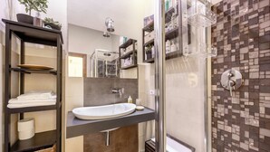 Een moderne badkamer met een douchecabine van glas, een wit wastafelmeubel en een plank met toiletartikelen.