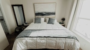 A bedroom with a bed, a bedside table, a mirror, and a window.