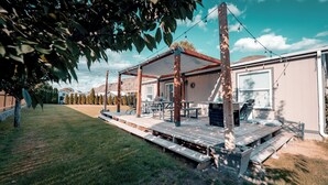 A covered outdoor patio with wooden benches and tables, a barbecue grill, and a string of lights. - The Sunland Hideaway -Spacious 4-bedroom house in tranquil Sunland Estates. (Quincy)