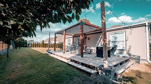 Un patio exterior techado con bancos y mesas de madera, una parrilla y una guirnalda de luces.