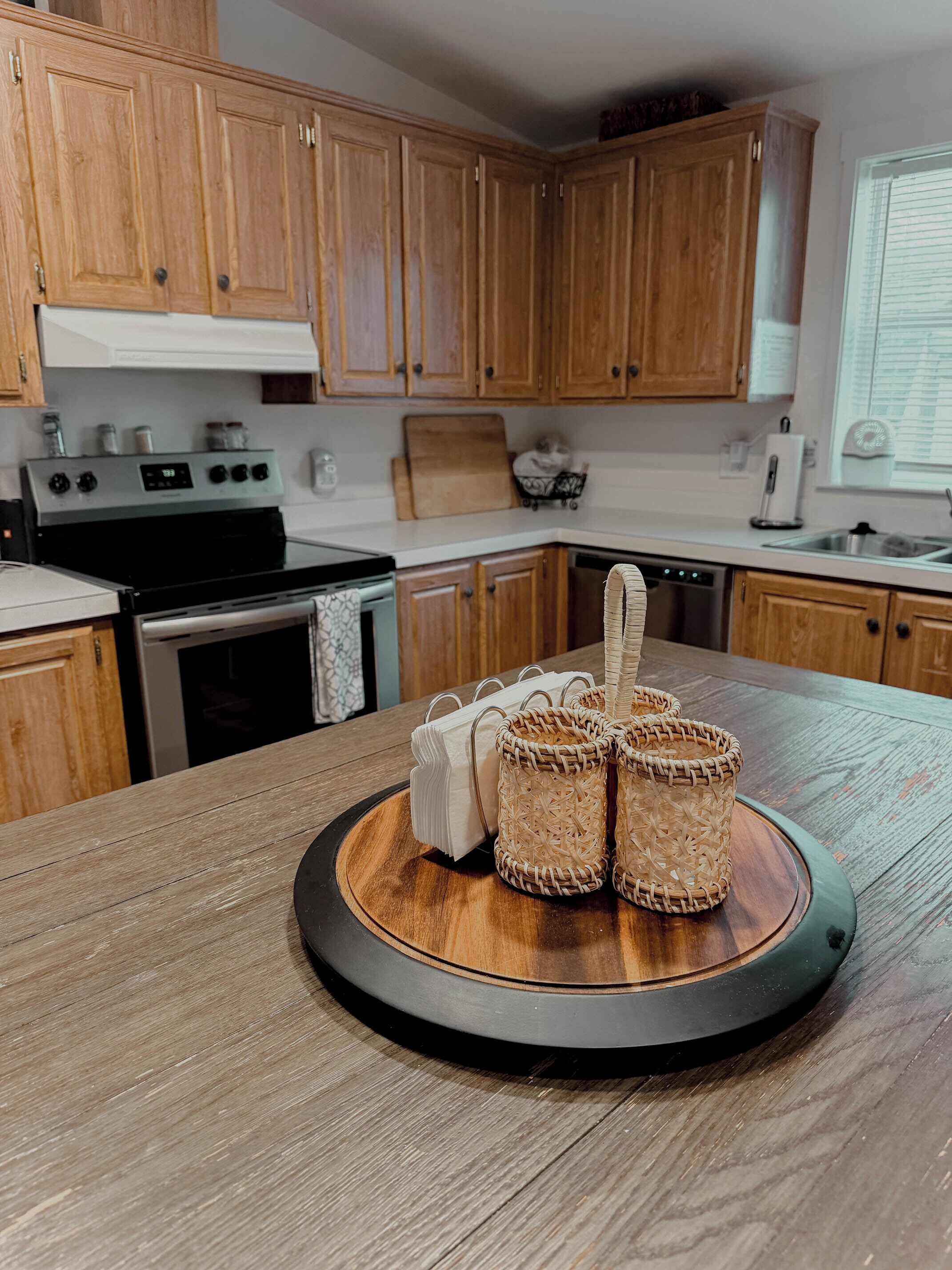 Une cuisine avec des meubles de rangement en bois, une cuisinière, un lave-vaisselle et une table ronde en bois sur laquelle sont posés des paniers en osier.