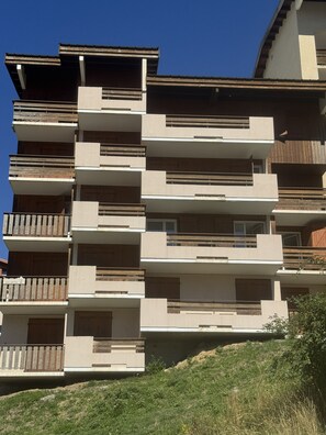 A multi-story residential building with balconies, a flat roof, and a hillside backdrop. - Spacious 105 m² apartment at the base of the slopes in the village of Les Deux Alpes 1800 (Les Deux Alpes)