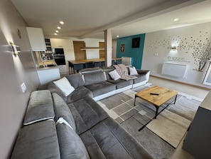 A modern living room with a sectional sofa, a coffee table, and a dining area with a kitchen in the background. - Spacious 105 m² apartment at the base of the slopes in the village of Les Deux Alpes 1800 (Les Deux Alpes)