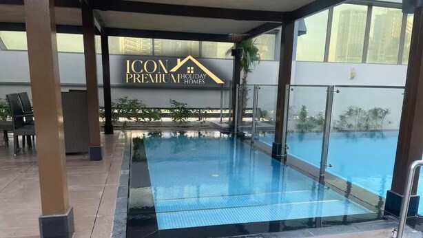 Area piscina con barriera in vetro, cartello per ICON PREMIUM Holiday Homes e vista sugli edifici circostanti.