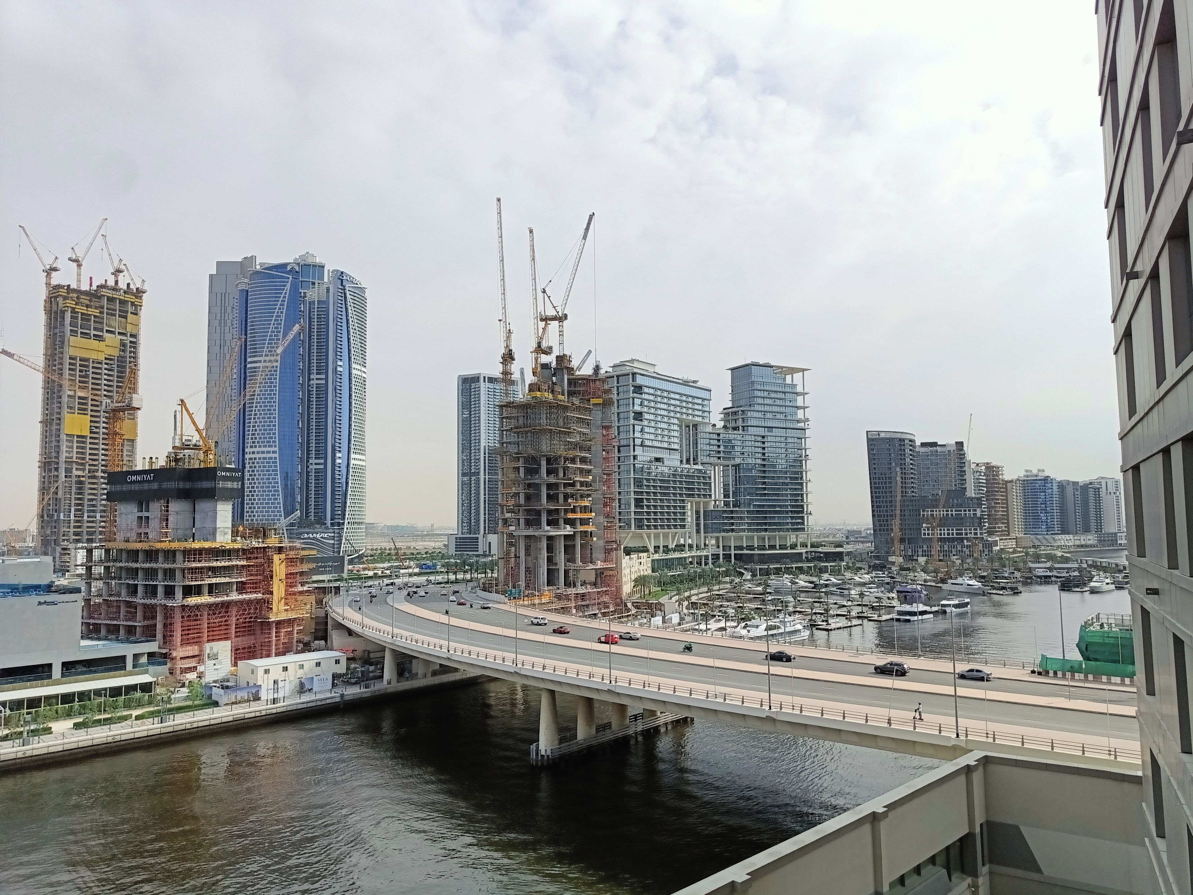 A cityscape with high-rise buildings, a bridge over water, and a marina with boats.