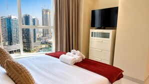 Una camera d'albergo con un letto, una televisione, una finestra che offre vista su edifici e un asciugamano rosso sul letto.