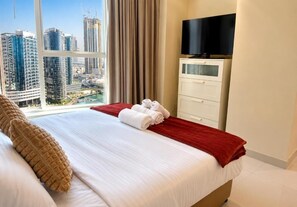 Ein Hotelzimmer mit Bett, Fernseher, Fenster mit Blick auf Gebäude und einem roten Handtuch auf dem Bett.