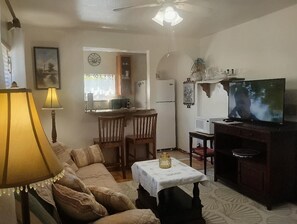 A living room with a sofa, a table with a lamp, a television, and a kitchen area in the background. - Charming Apartment in a Serene Location  Close to FIT & Everything (Melbourne)