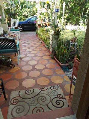 A tiled pathway leading to a seating area with a bench and chairs, surrounded by potted plants and a blue car parked nearby. - Charming Apartment in a Serene Location  Close to FIT & Everything (Melbourne)