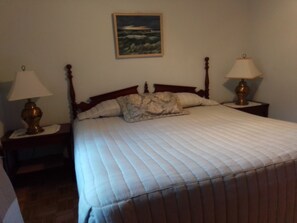 A bedroom with a bed, two bedside tables with lamps, a painting on the wall, and a wooden headboard. - Charming Apartment in a Serene Location  Close to FIT & Everything (Melbourne)