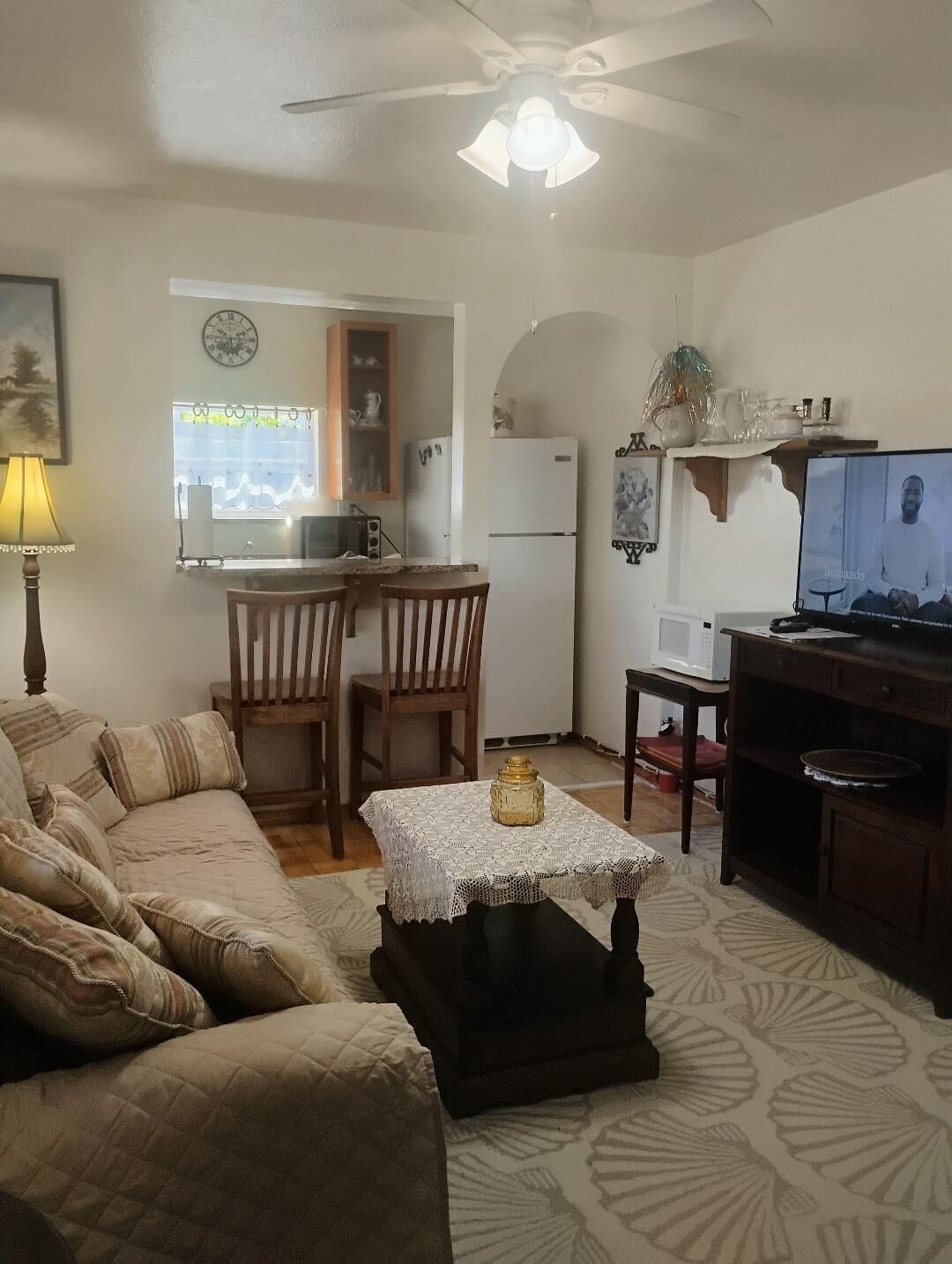 Uma sala de estar com sofá, mesa de centro, televisão e área de cozinha com frigorífico, micro-ondas e mesa de jantar.