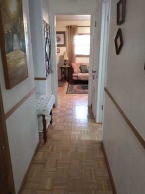 A hallway with a wooden floor leading to a room with a bed, a lamp, and a window with curtains. - Charming Apartment in a Serene Location  Close to FIT & Everything (Melbourne)