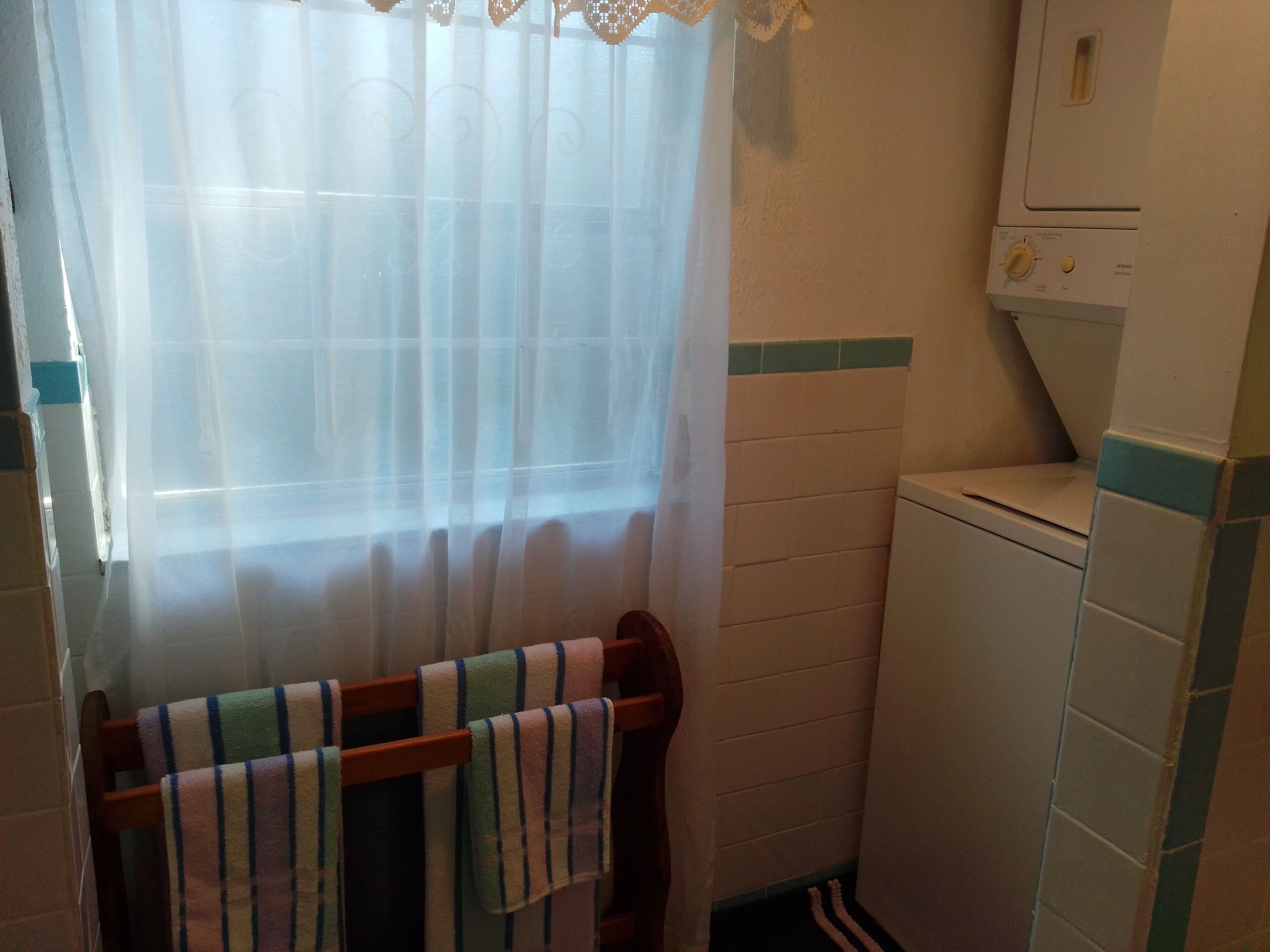 Un baño con inodoro, toallero y toallas a rayas, y una ventana con cortina translúcida.