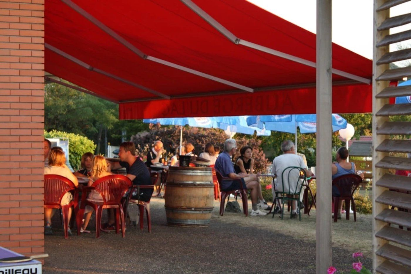 Un espace extérieur aménagé avec des chaises et des tables rouges, un tonneau en bois et un auvent rouge.