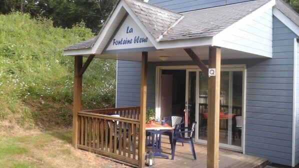 A small building with a sign reading 'La Fontaine Glene' and a covered outdoor seating area with a table and chairs.