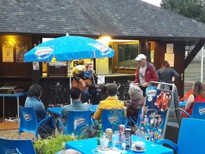 An outdoor seating area with tables and chairs, some with blue covers, and a blue umbrella with a logo.