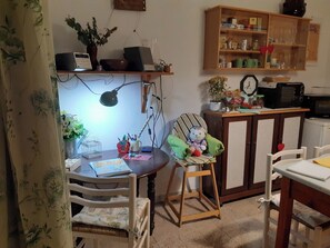 Ein gemütliches Zimmer mit Holztisch, Schaukelstuhl, Schreibtisch mit Computer und einer Küchenzeile.