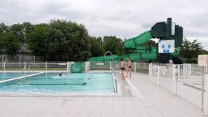 Une piscine avec un toboggan aquatique vert et une zone délimitée par une clôture.