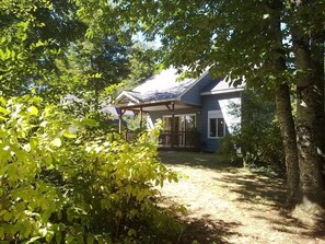 Une maison dotée d’un porche abrité, entourée d’une végétation luxuriante et d’arbres.