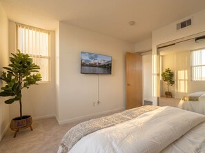 Una camera da letto con un letto, una TV a parete, una finestra con persiane e una porta.