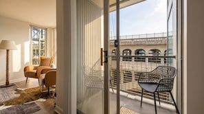 A room with a sliding glass door leading to a balcony with a view of a bridge and arches. There are two chairs on the balcony. - Luxury 2BR Apartment Balcony, Gym & Parking (Cleveland)