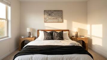A bedroom with a bed, two bedside tables, lamps, a wall art piece, and a window.