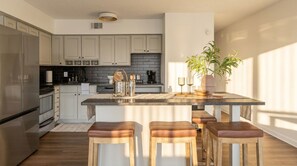 A modern kitchen with a central island, bar stools, and a potted plant. - Luxury 2BR Apartment Balcony, Gym & Parking (Cleveland)