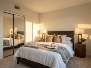 Une chambre à coucher avec un grand lit, des lampes de chevet, un miroir et une petite table d’appoint sur laquelle est posée une plante.