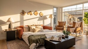 A modern bedroom with a large bed, two chairs, a coffee table, and a view of a bridge. - Luxury 2BR Apartment Balcony, Gym & Parking (Cleveland)