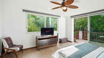 A bedroom with a bed, a TV, a ceiling fan, a chair, a dresser, and a sliding glass door leading to a balcony.