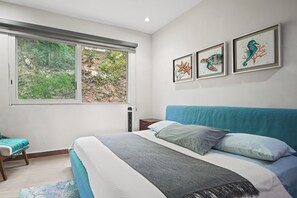 Quarto com uma cama, mesa de cabeceira, janela com vista para o verde e três quadros na parede.