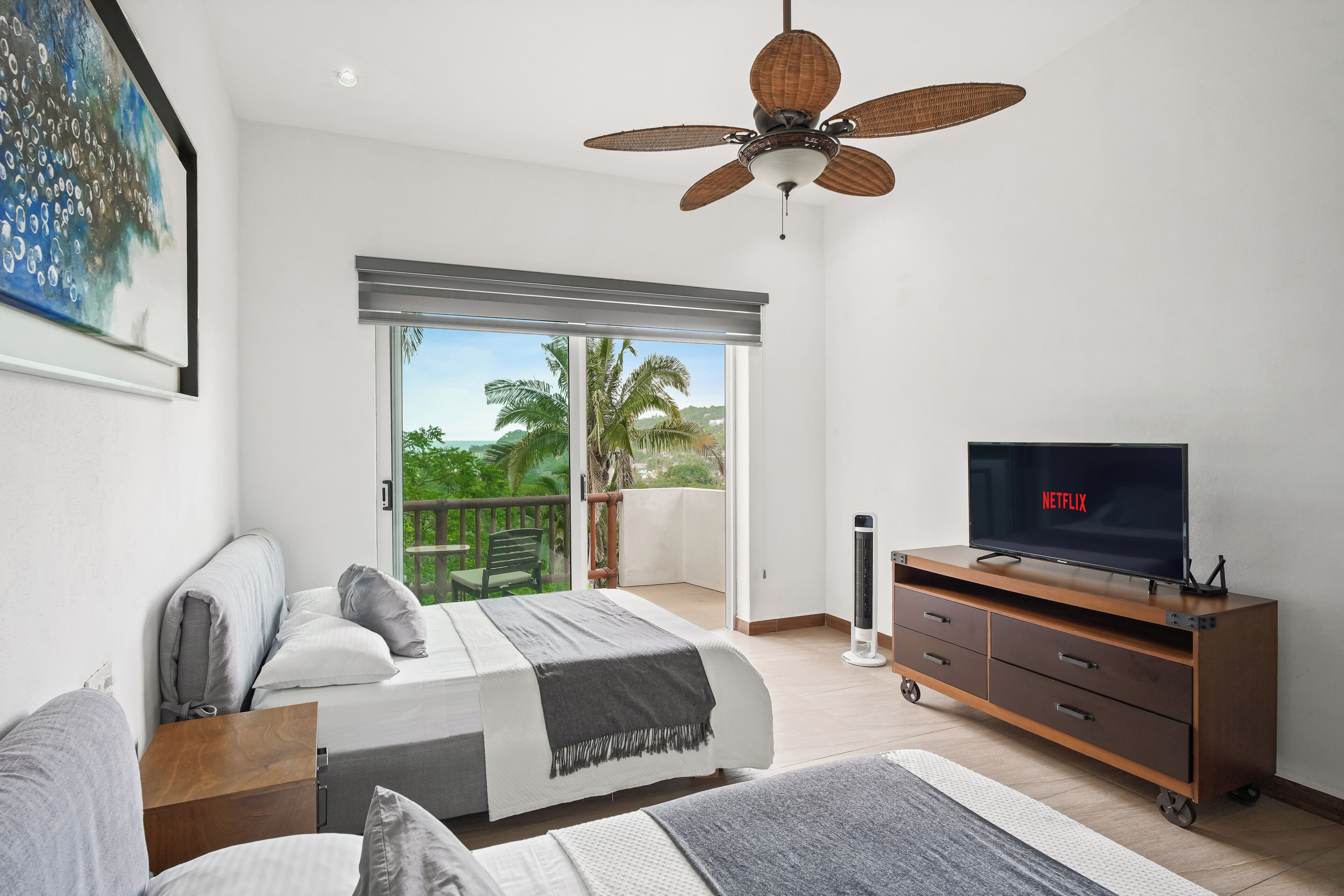 Un dormitorio con cama, televisor, ventilador de techo y balcón con vistas a zonas verdes.