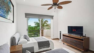 Un dormitorio con cama, televisor, ventilador de techo y balcón con vistas a zonas verdes.