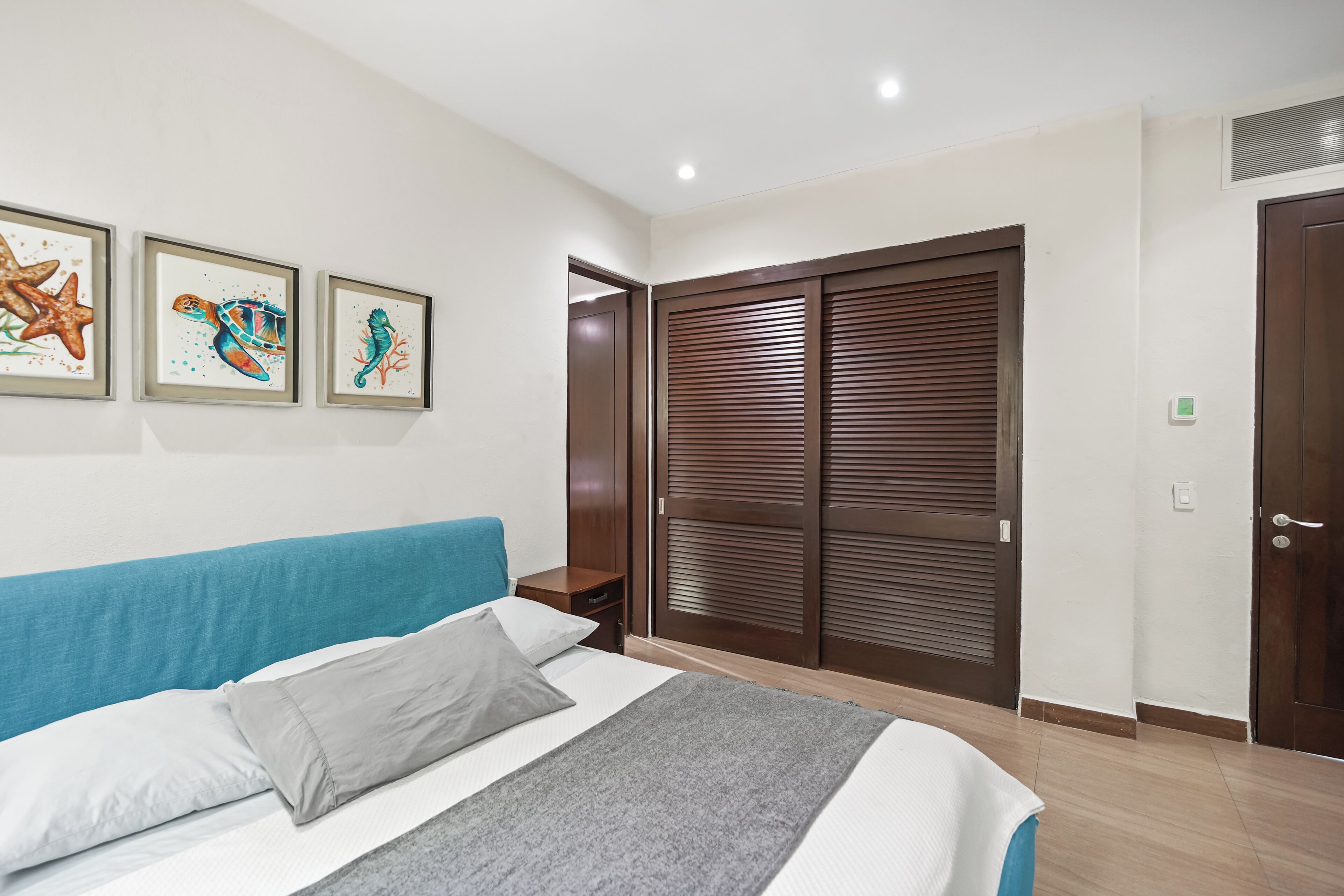 A bedroom with a bed, a nightstand, a wardrobe, and three framed seahorse paintings on the wall.