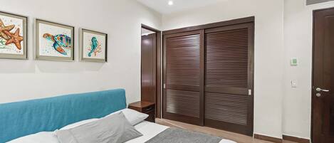 A bedroom with a bed, a nightstand, a wardrobe, and three framed seahorse paintings on the wall.