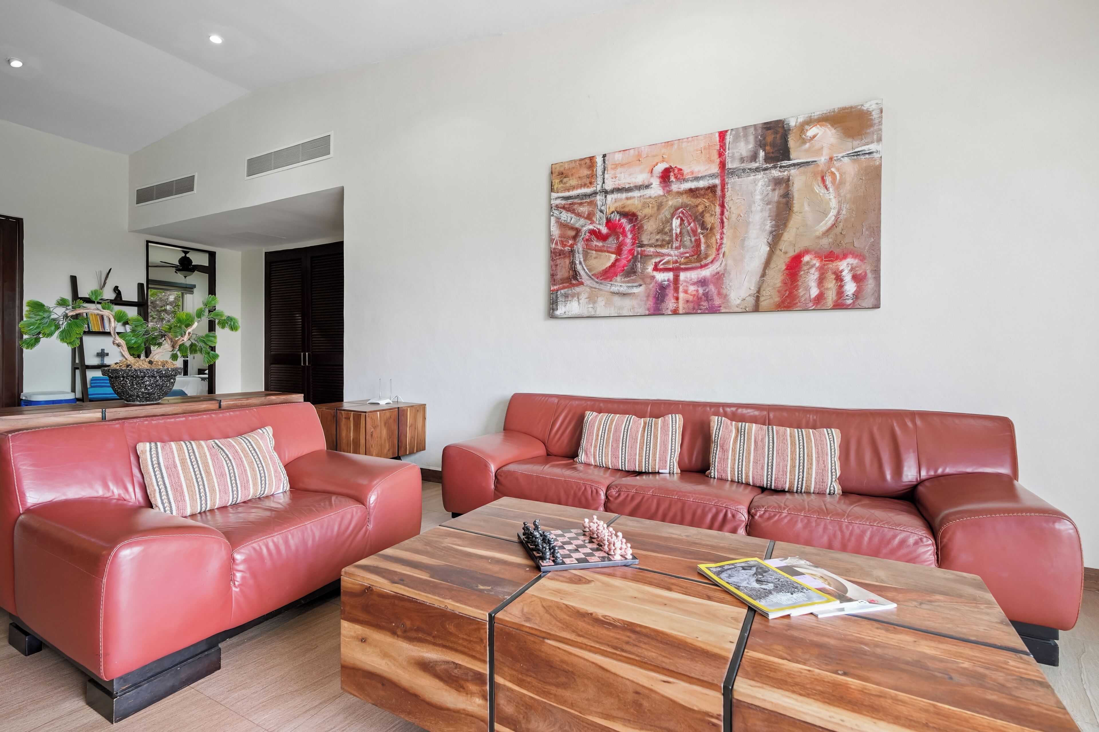 Una sala de estar moderna con un sofá de cuero rojo, una mesa de centro de madera y un cuadro abstracto grande en la pared.