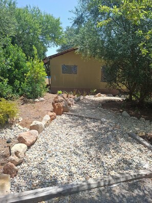 A building with a gravel pathway leading to it, surrounded by trees and rocks.
